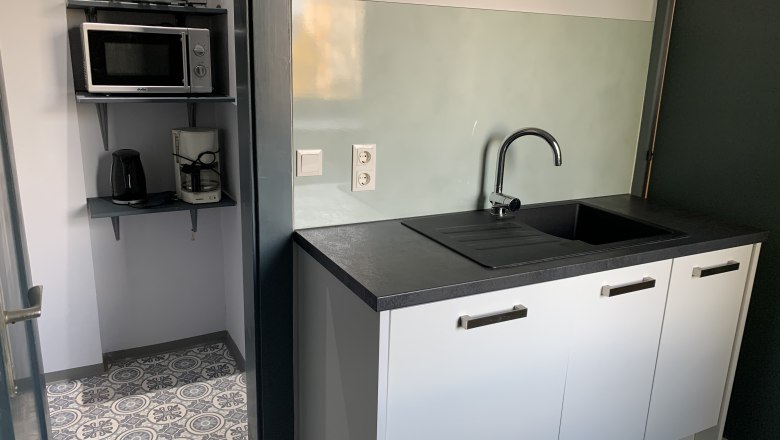 Small kitchen with sink, microwave, toaster and coffee machine.