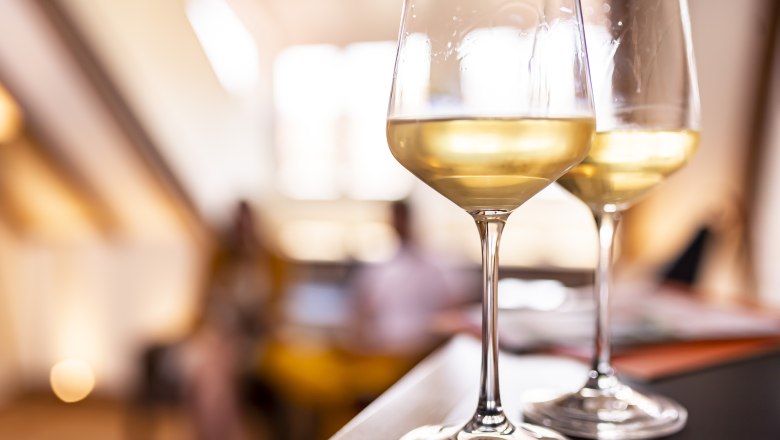 Two glasses of white wine on a table, blurred background.