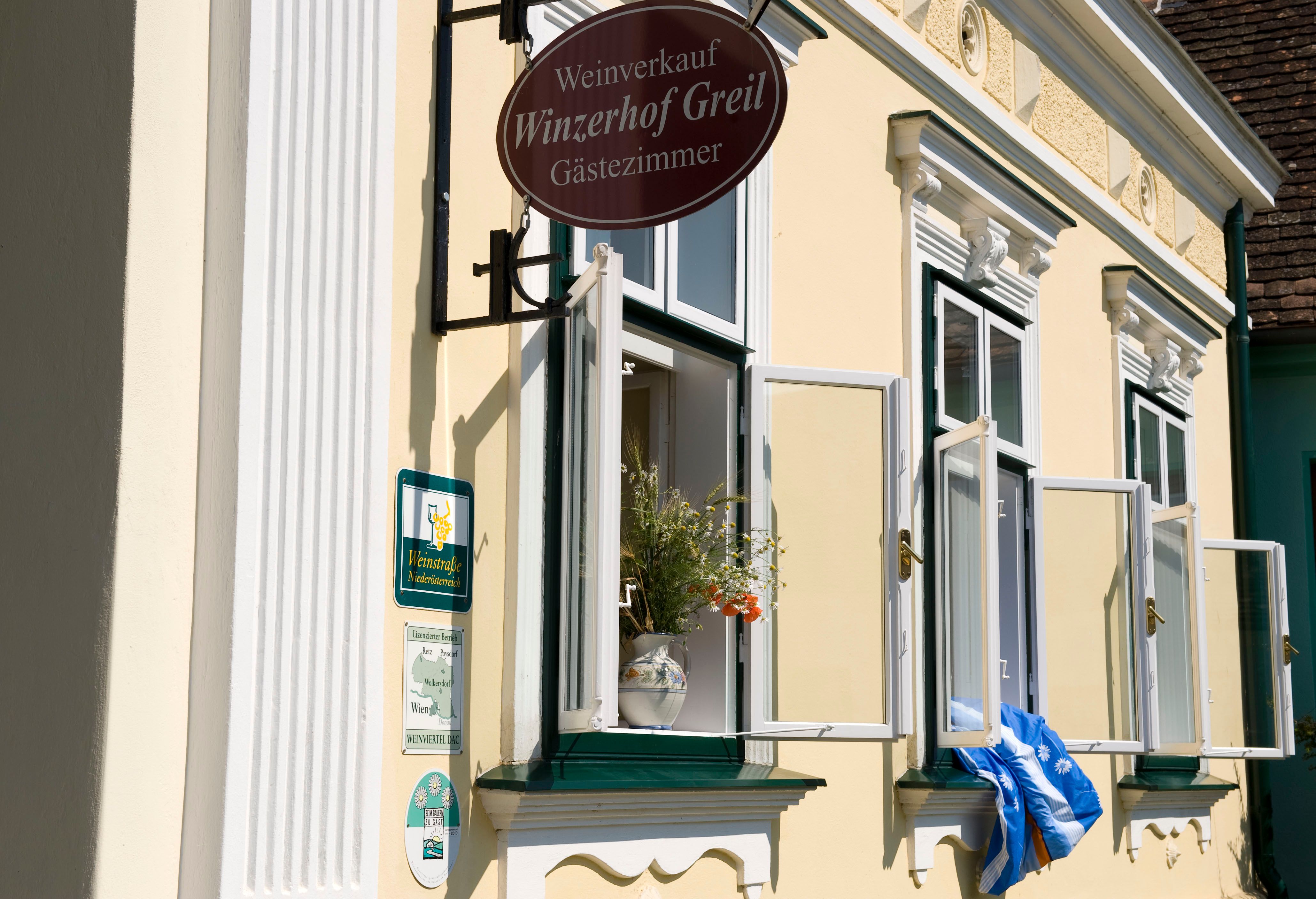 Facade of a yellow building with open windows and a sign 'Winzerhof Greil'.