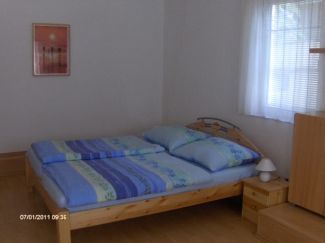 A simply furnished bedroom with a double bed, a bedside table and a window with curtains.