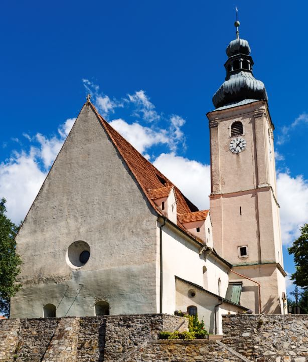 Wiesmath parish church with tower, stone cemetery wall and clock against a blue sky.