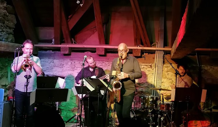 A jazz band plays in a rustic room with wooden beams and stone walls.