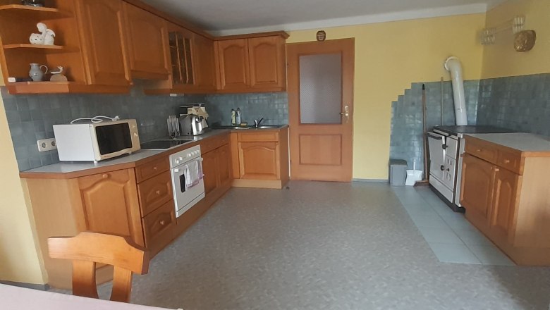 A spacious eat-in kitchen with wooden furniture, a dining table, stove, microwave and yellow walls.