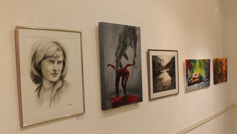 Five works of art hang on a white wall in a gallery.