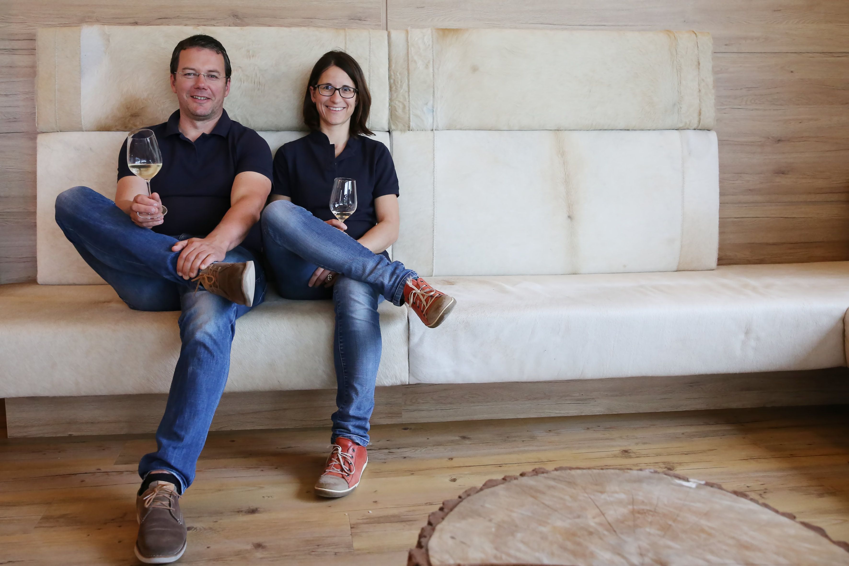 A man and a woman are sitting on a sofa holding glasses of wine.