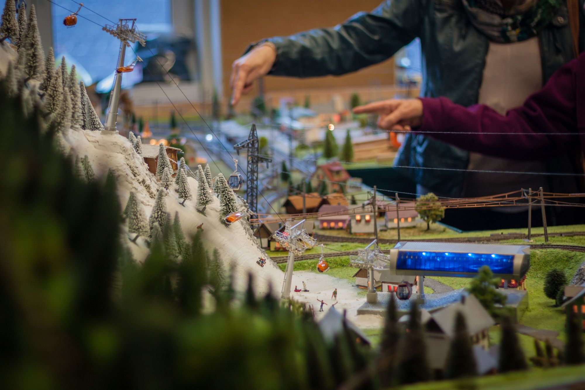 Detailed model landscape with cable car and snow-covered trees, two people pointing at the model in the background.