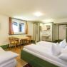 A simply furnished hotel room with a double bed, table, chairs, TV and washing area.