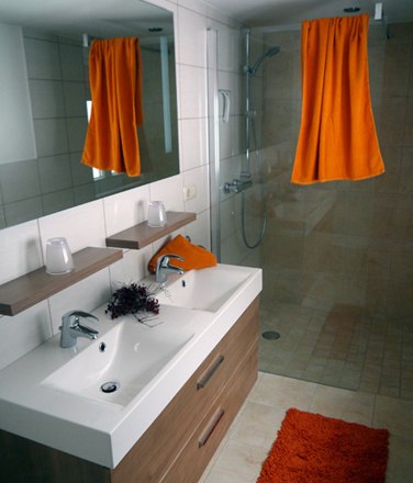 Modern bathroom with double washbasin, large mirror, shower and orange accents.