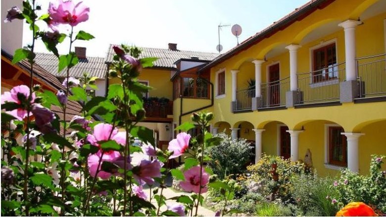 A sunny courtyard with a yellow building, white columns and blooming pink flowers in the foreground.