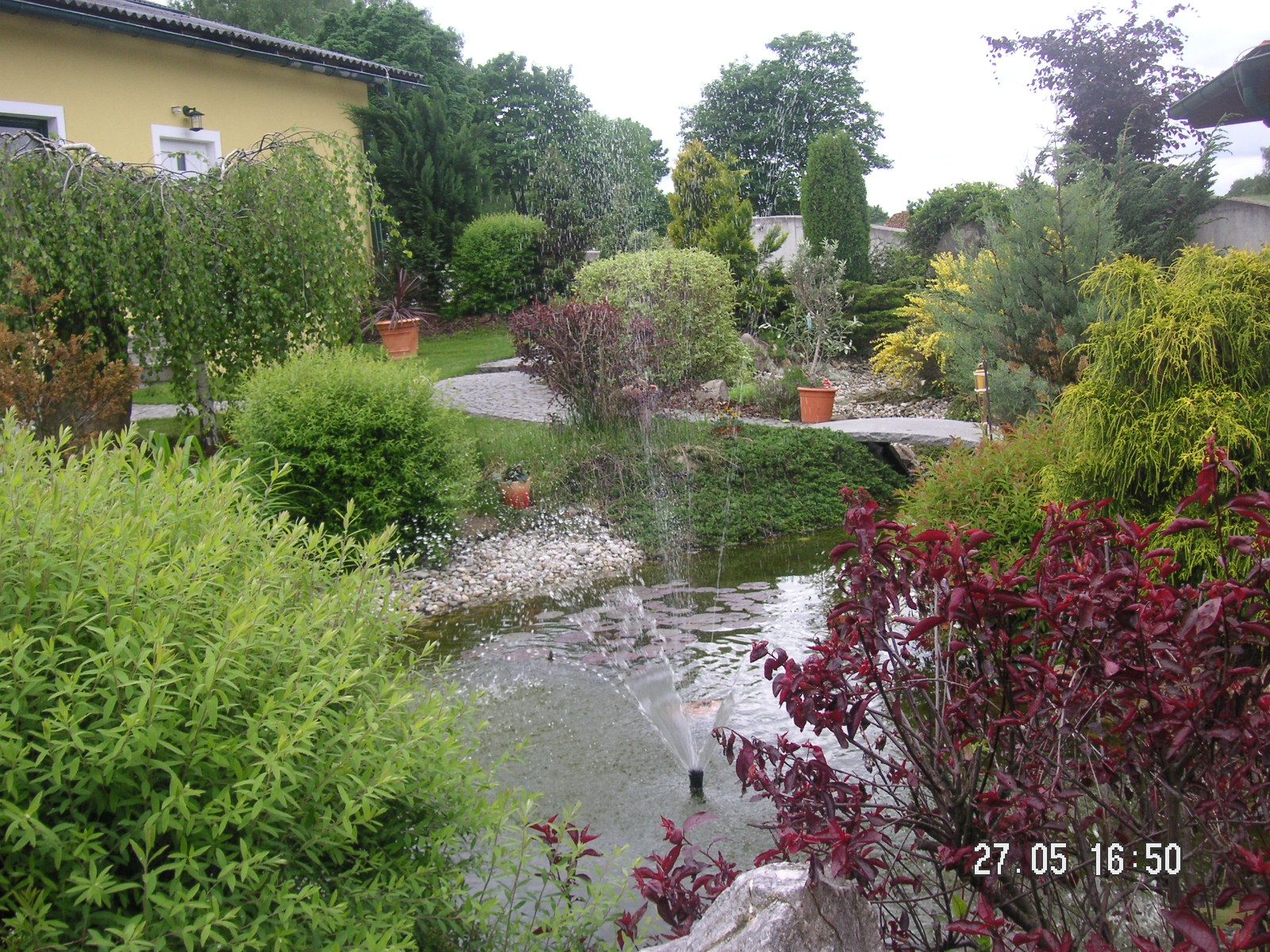 A well-tended garden with a pond, fountain and lush vegetation.