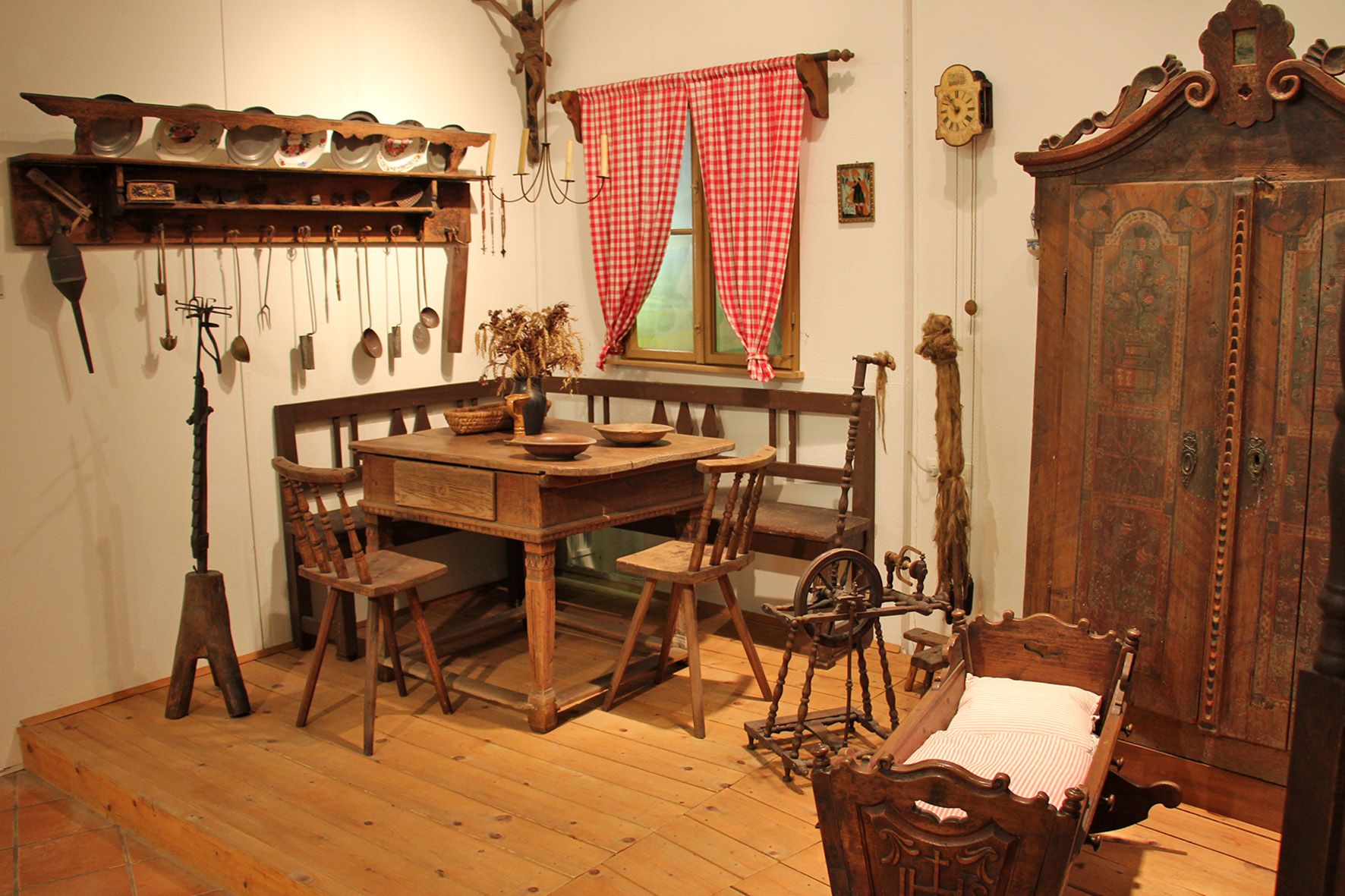 Historic farmhouse parlor with wooden furniture, spinning wheel and cradle.