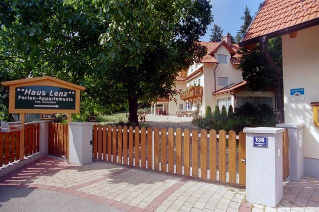 Entrance to Haus Lenz with wooden fence and sign, surrounded by trees.