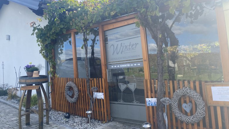 Entrance of a building with wooden paneling and vines, decorated with wreaths and a table with flowers.