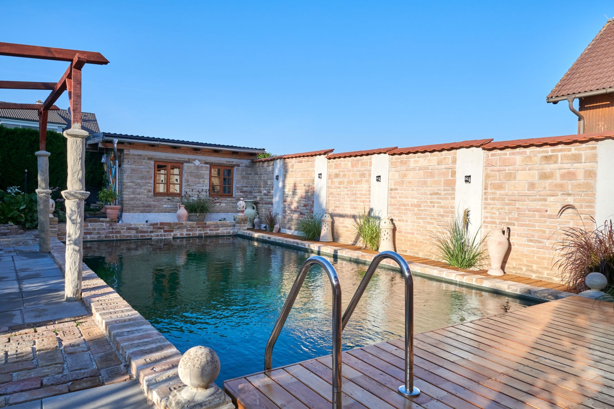 A small pool with a wooden deck and brick walls in the background.