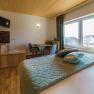 Comfortable hotel room with wooden floor, double bed, small table and chairs, TV and large window with a view.
