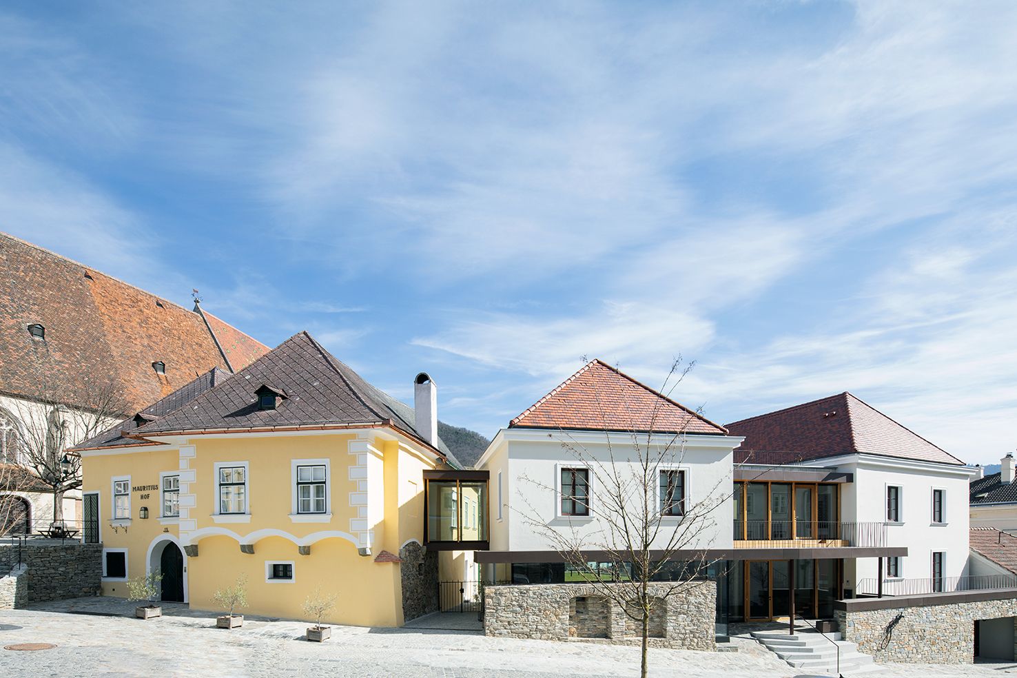 Two buildings with yellow and white façades, connected by a modern glass corridor, under a blue sky.