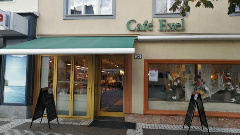 Exterior view of Café Exel with green awning and shop window decoration.