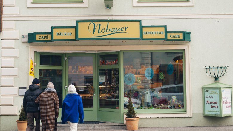 In the wintry atmosphere, visitors stroll relaxed to the charming patisserie with its inviting windows and warm light. The aroma of freshly baked treats wafts through the cold air and promises sweet delights, while the snow-capped mountains in the background provide a picturesque backdrop.