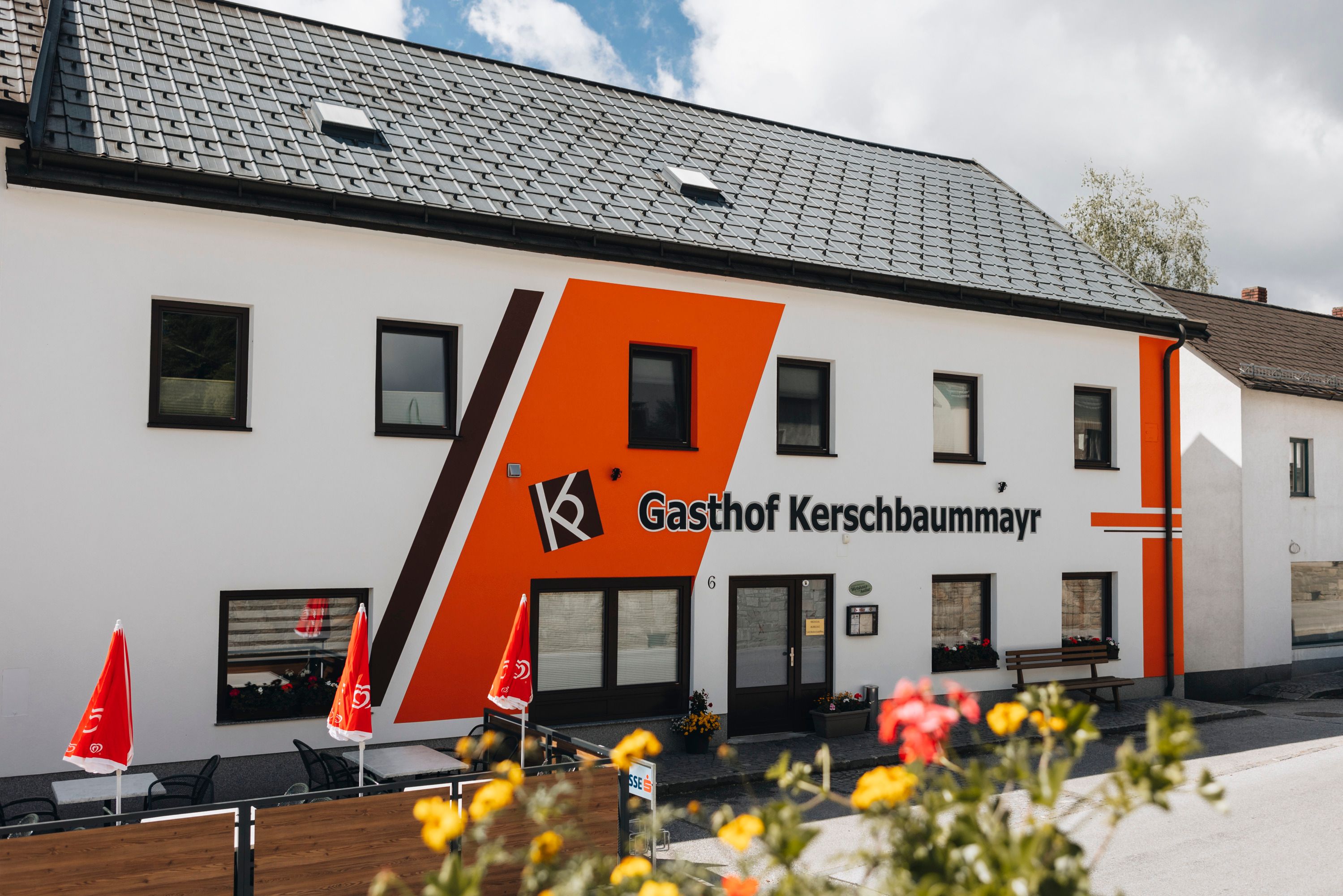 Exterior view of the Gasthof Kerschbaummayr with orange façade and red parasols.