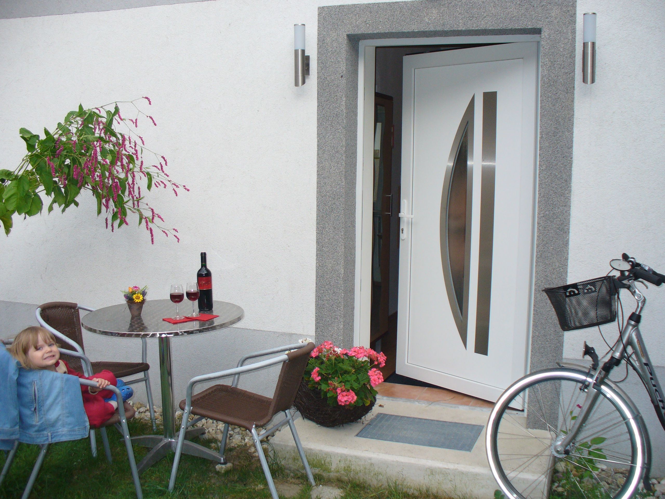 An open house entrance with table, chairs, wine bottle and bicycle.
