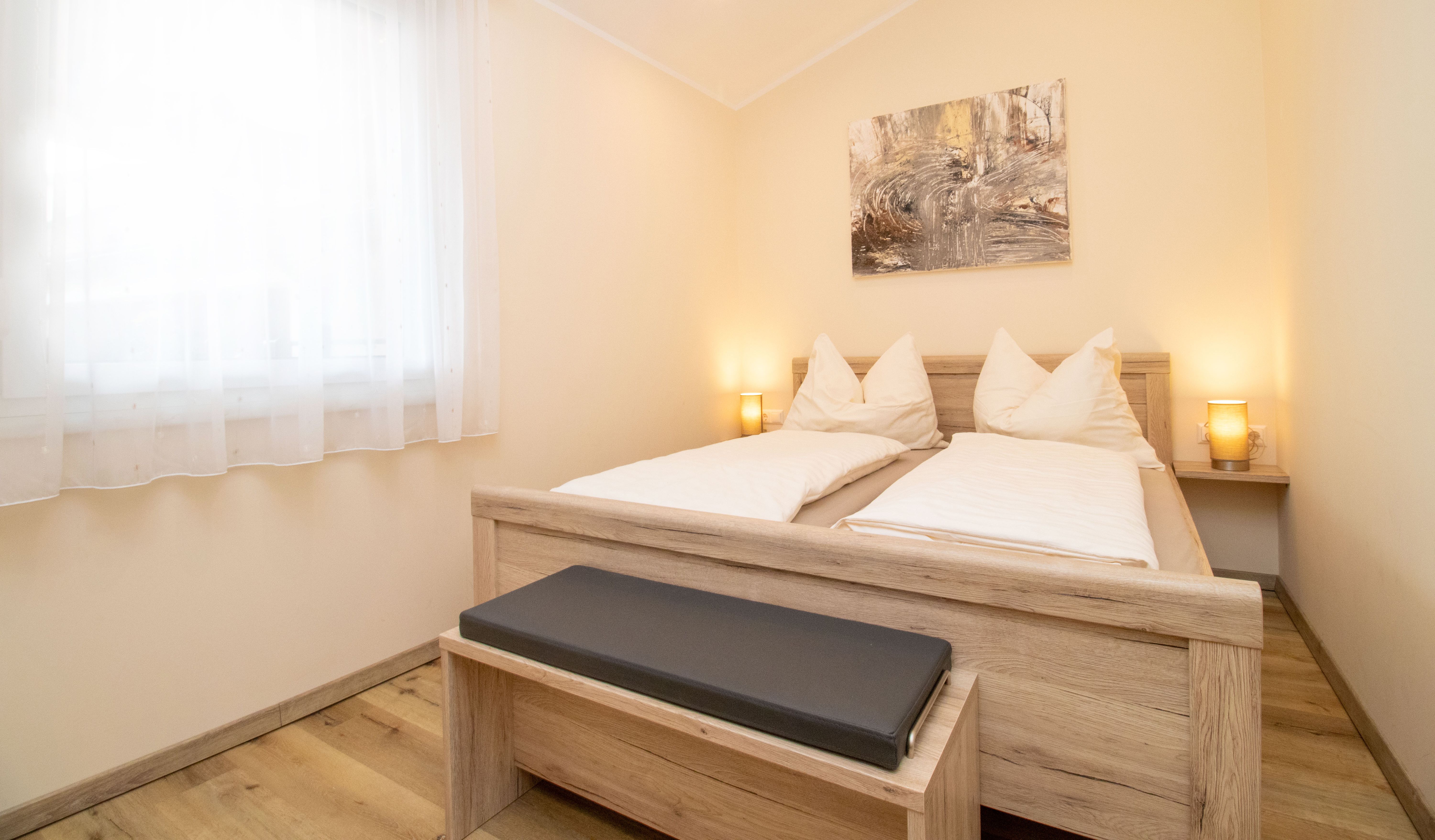 A cozy bedroom with a wooden double bed, two bedside lamps, and a picture on the wall.