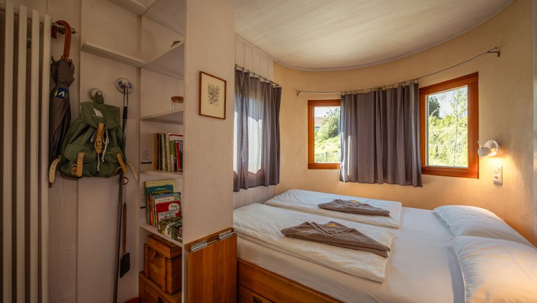 Interior view of a cozy bedroom with double bed, shelves and windows with curtains.