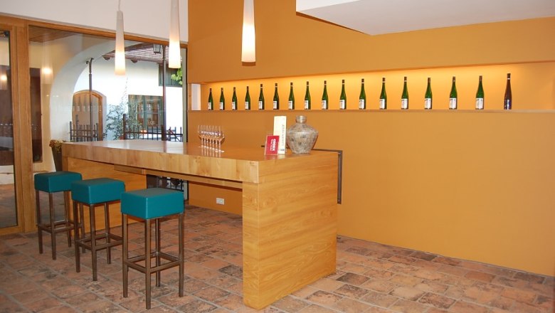 Modern tasting room with wooden counter, bar stools and wine bottles on the wall.