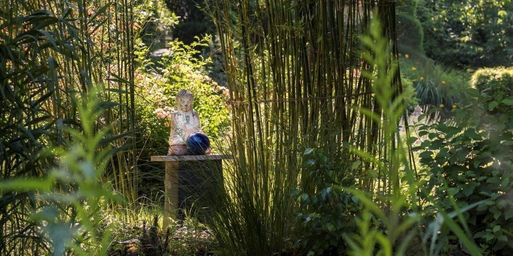 An Asian-inspired garden with a Buddha statue on a table, surrounded by bamboo and lush greenery.