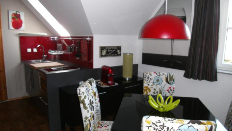 Modern kitchen with red splashback, dining table and patterned chairs.