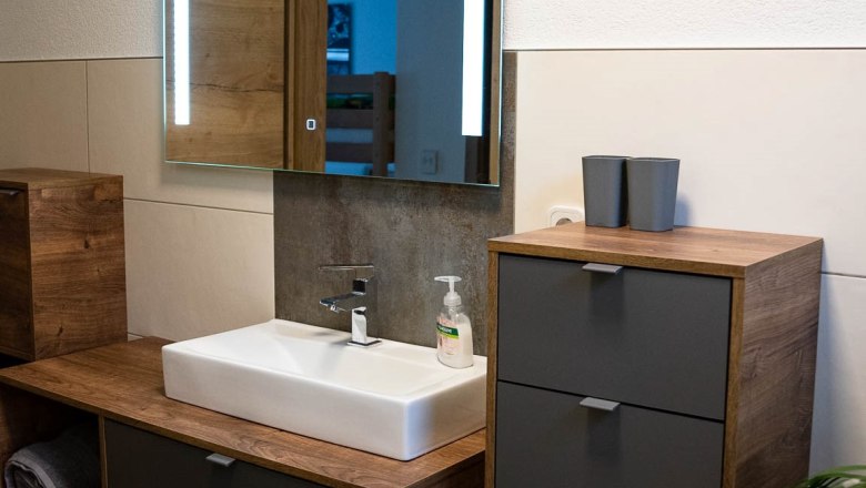 Modern bathroom with wooden cabinets, washbasin and illuminated mirror.