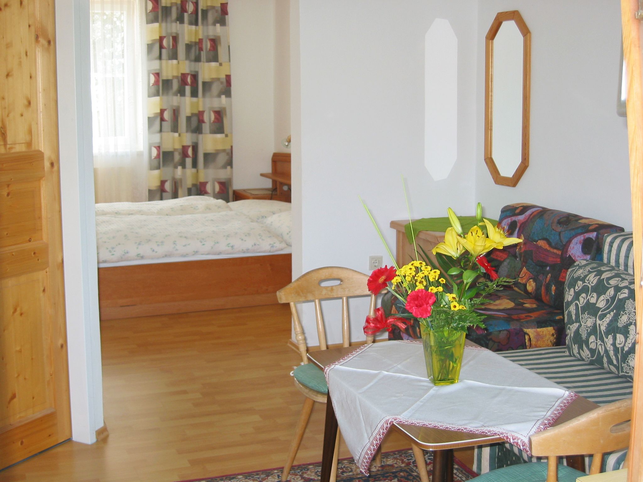 A cozy room with wooden furniture, a bed in the background and a table with flowers in the foreground.