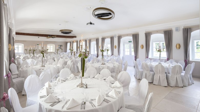 Elegant ballroom with white tables and chairs, decorated with candlesticks and flowers.