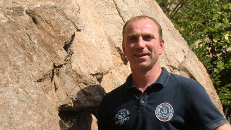 A man stands in front of a large rock and smiles at the camera.