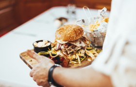 A burger with a sesame bun, bacon and fried egg on a wooden board, served with chips and dips.