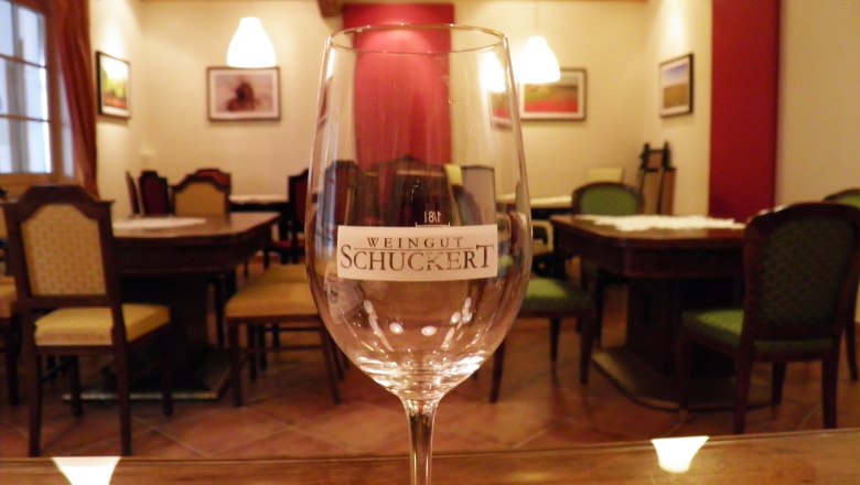 Wine glass with the inscription "Weingut Schuckert" in a cozy room with wooden furniture and pictures on the wall.