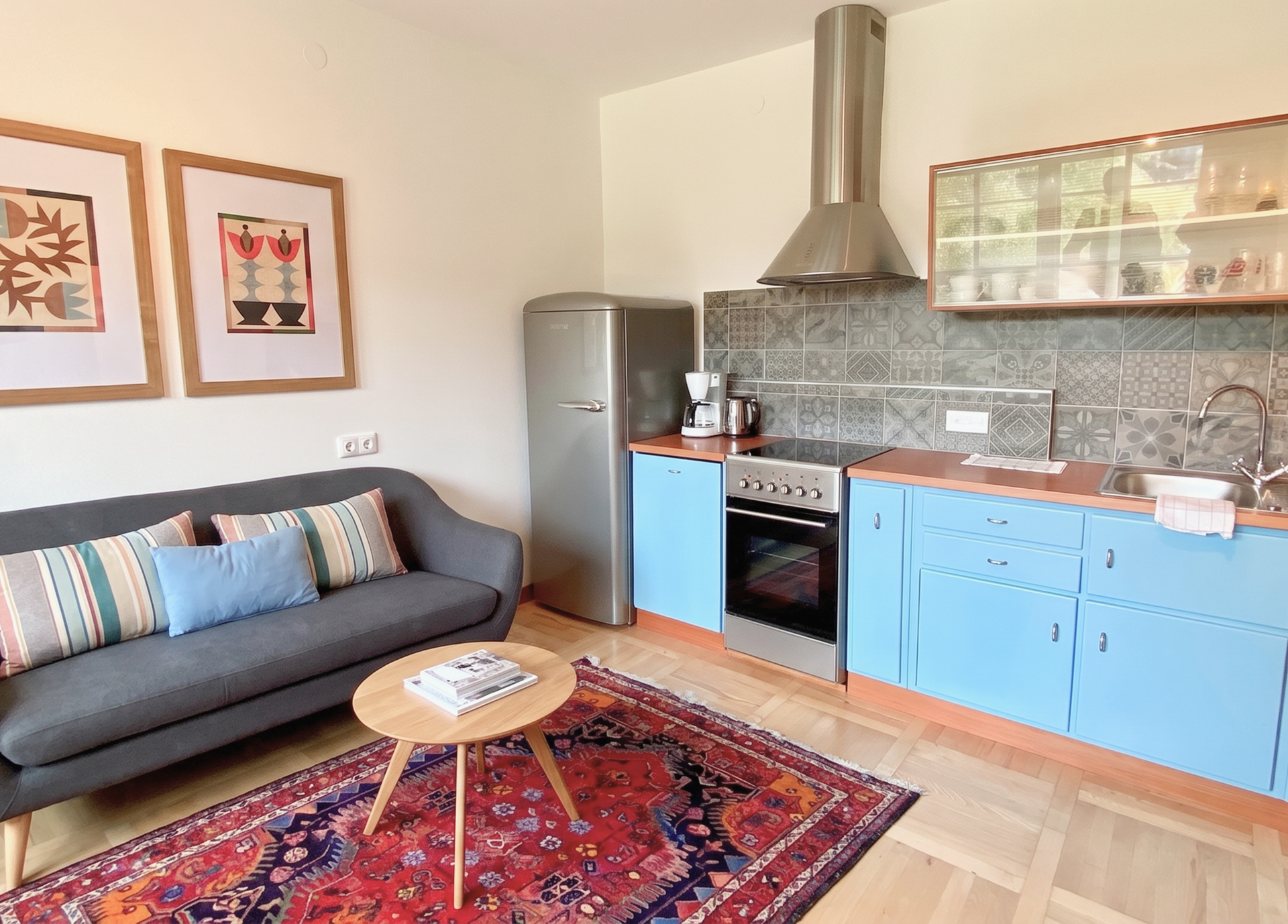 A cozy kitchen with blue cabinets, a gray sofa, and a colorful rug.
