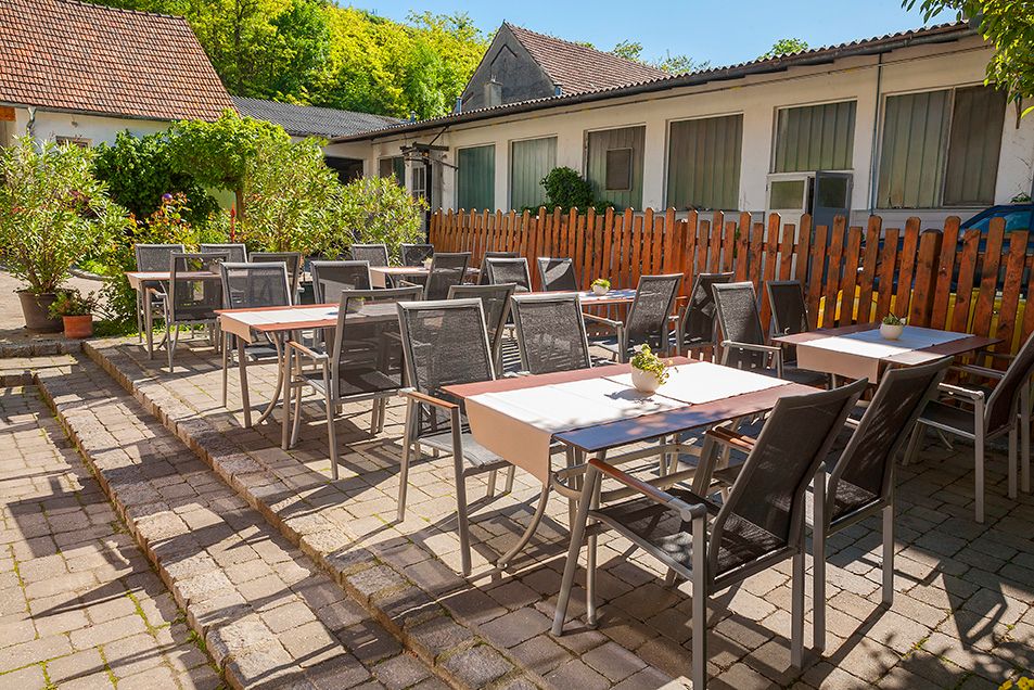 Outdoor dining area with tables and chairs, surrounded by plants and a wooden fence.