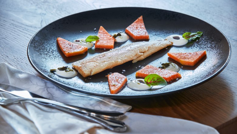 A plate with smoked trout, pieces of pumpkin and sheep's cheese cream, decorated with herbs.