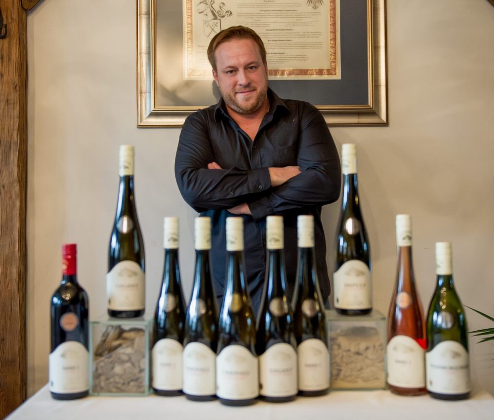 Man standing behind a row of wine bottles on a table.
