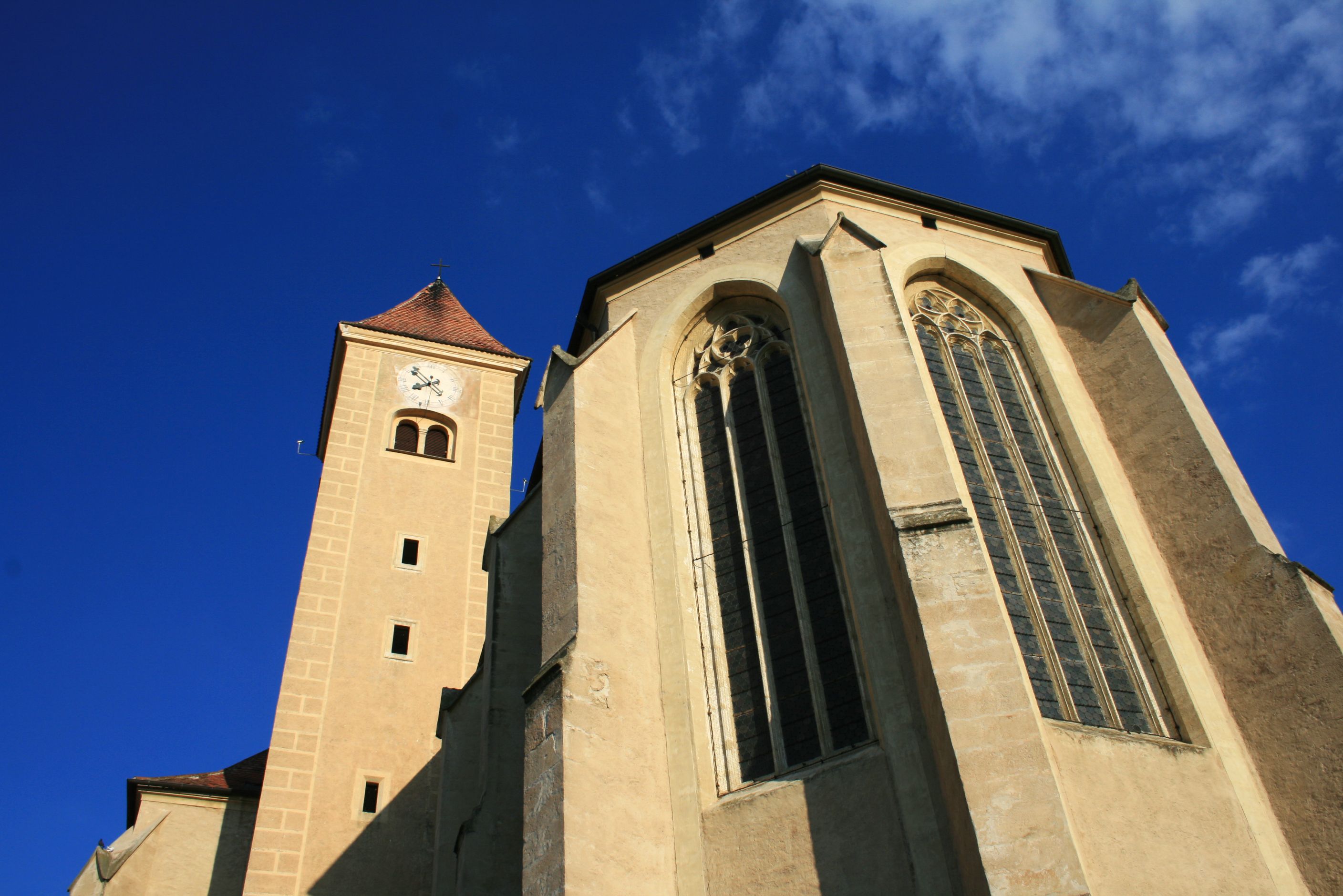View of the Church of the Holy Blood in Pulkau with tower and Gothic windows against a blue sky.