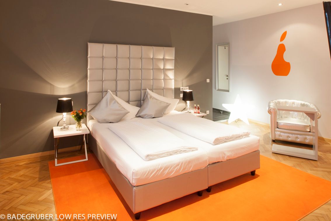 Modern hotel room with double bed, orange wall decoration and stylish armchair.