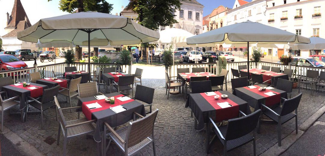 Outdoor terrace of a café with tables and parasols on a paved square.
