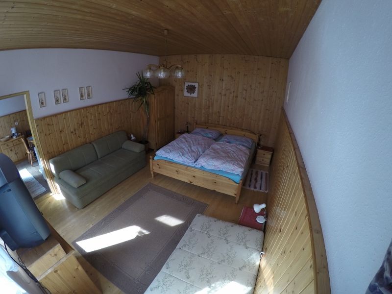 A cozy bedroom with wooden walls, a double bed, a sofa and a carpet on a wooden floor.