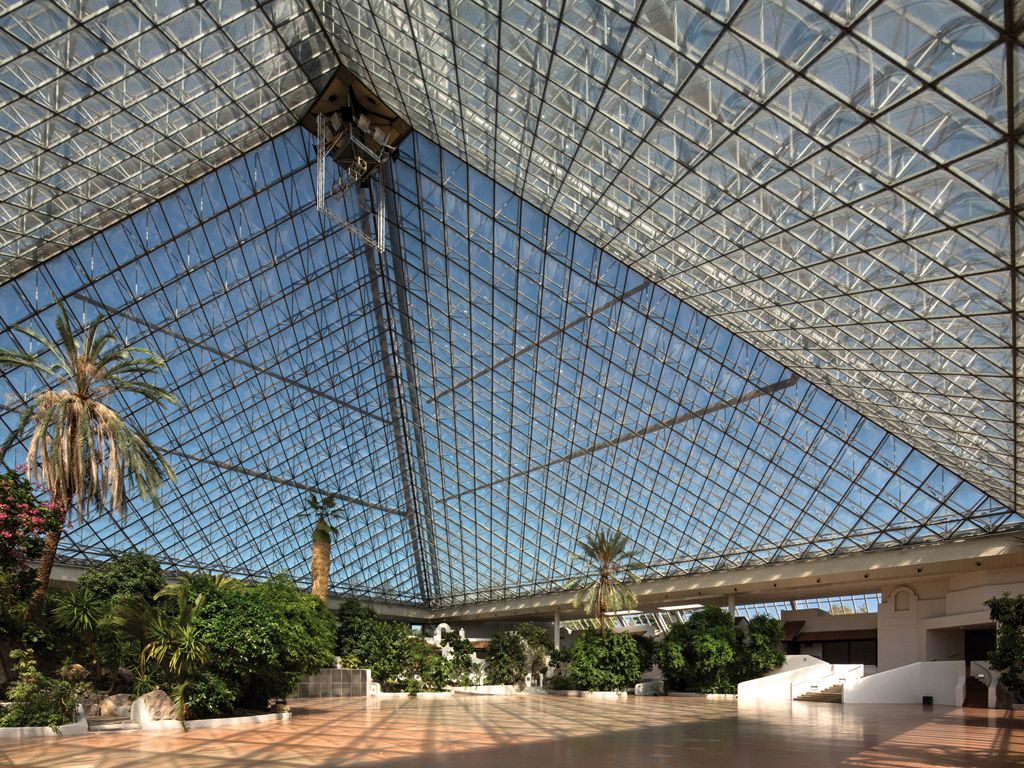 Interior view of a large glass pyramid with plants and palm trees.
