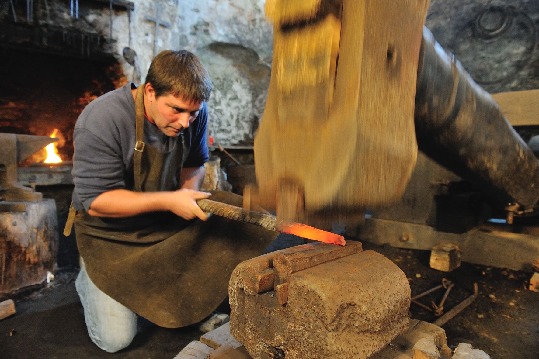A blacksmith works on red-hot metal with a hammer in a workshop.
