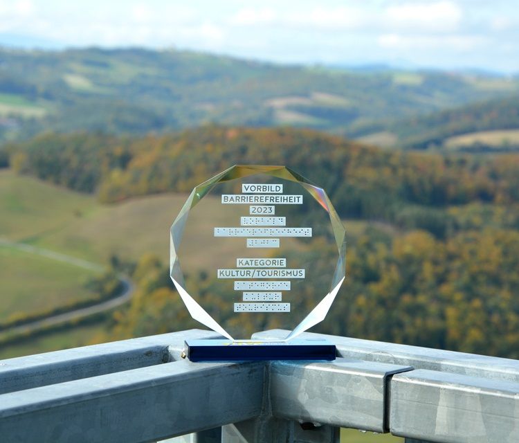 An award for accessibility 2023 stands on a railing with a landscape in the background. The viewing platform is accessible by elevator.