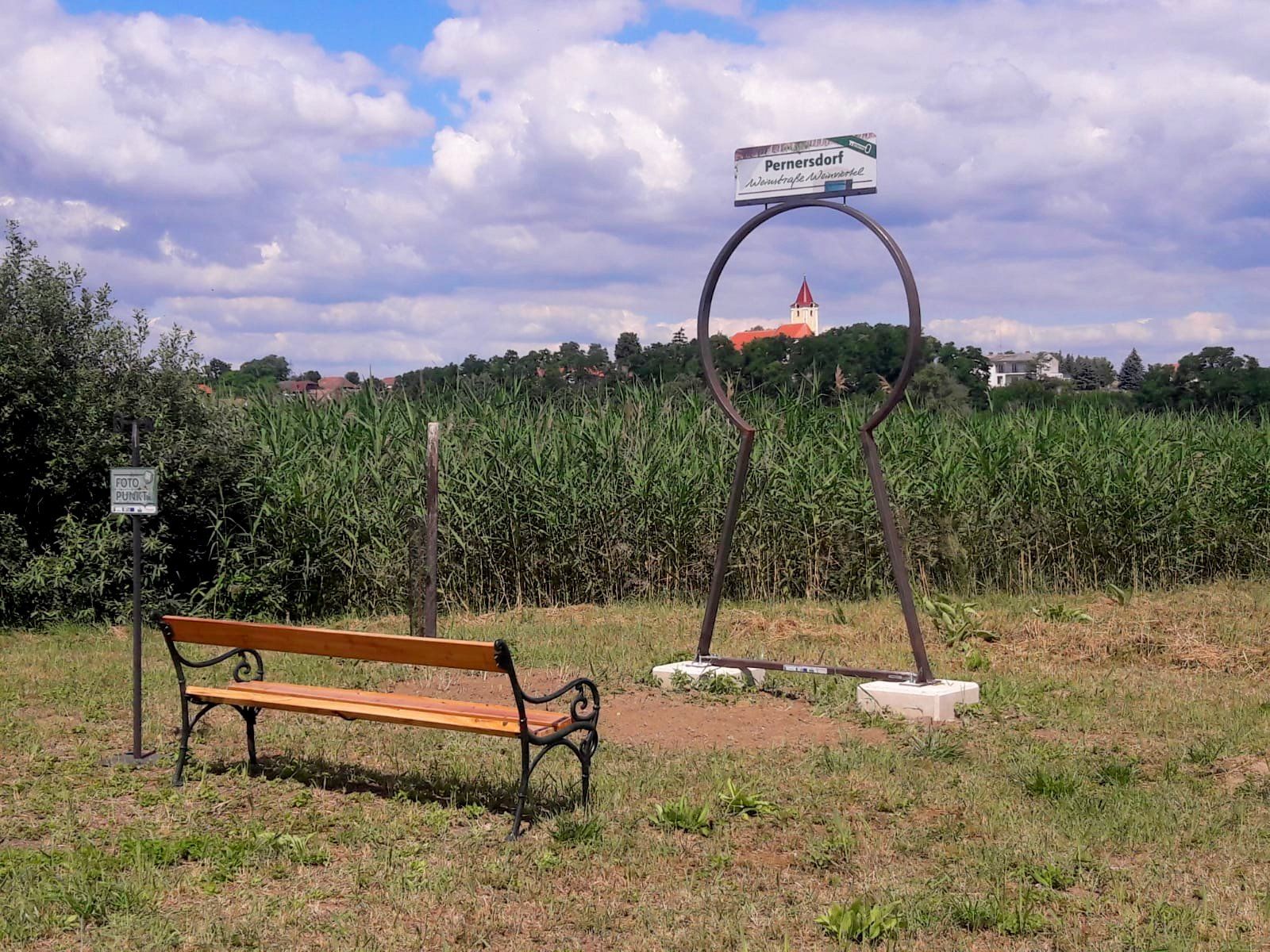 A bench in front of a photo point with a view of a church in Pernersdorf.