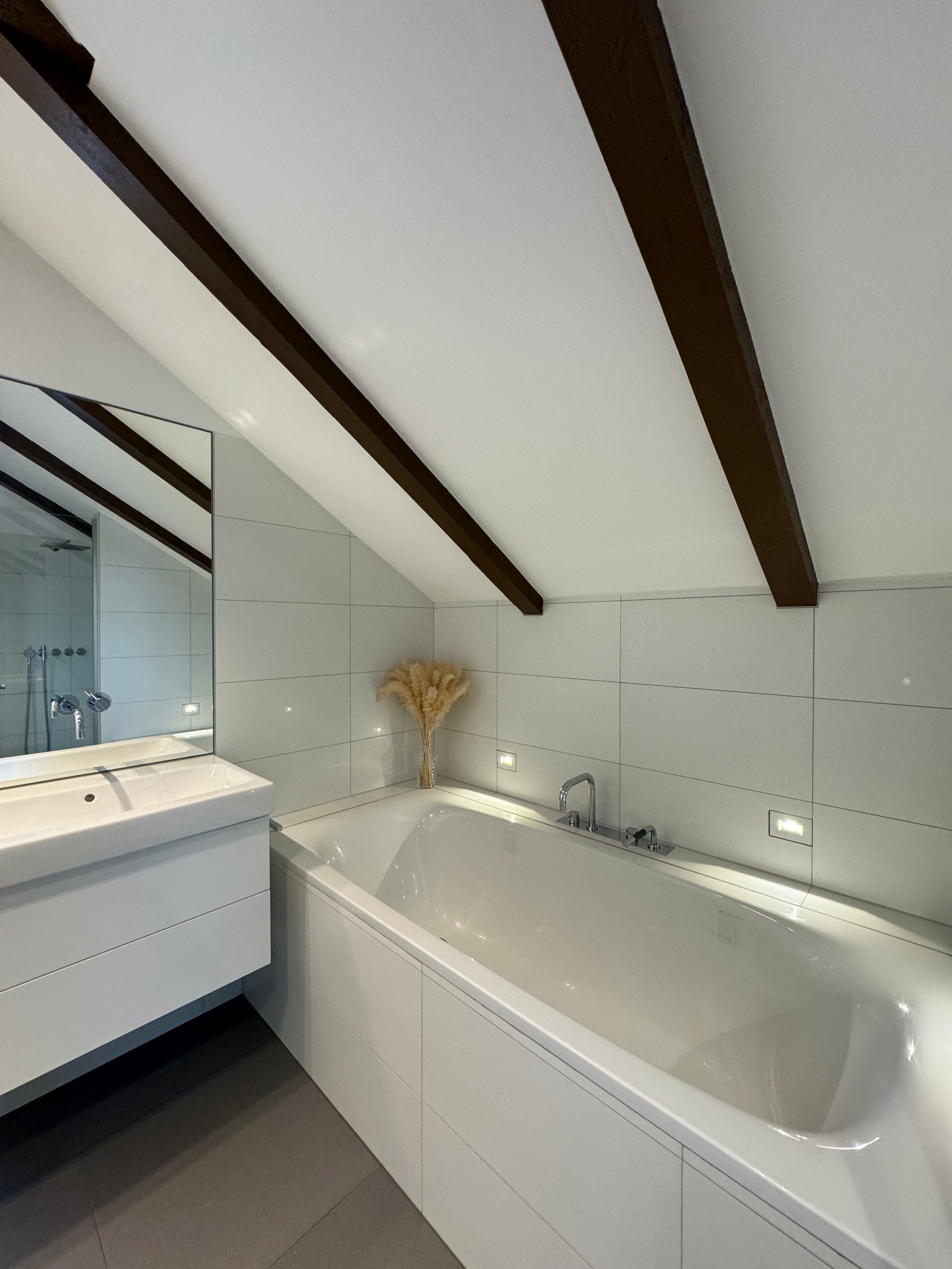 Modern bathroom with bathtub, washbasin and sloping ceiling with wooden beams.
