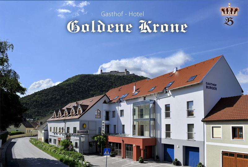 Gasthof-Hotel Goldene Krone in front of a wooded hill with a castle in the background.