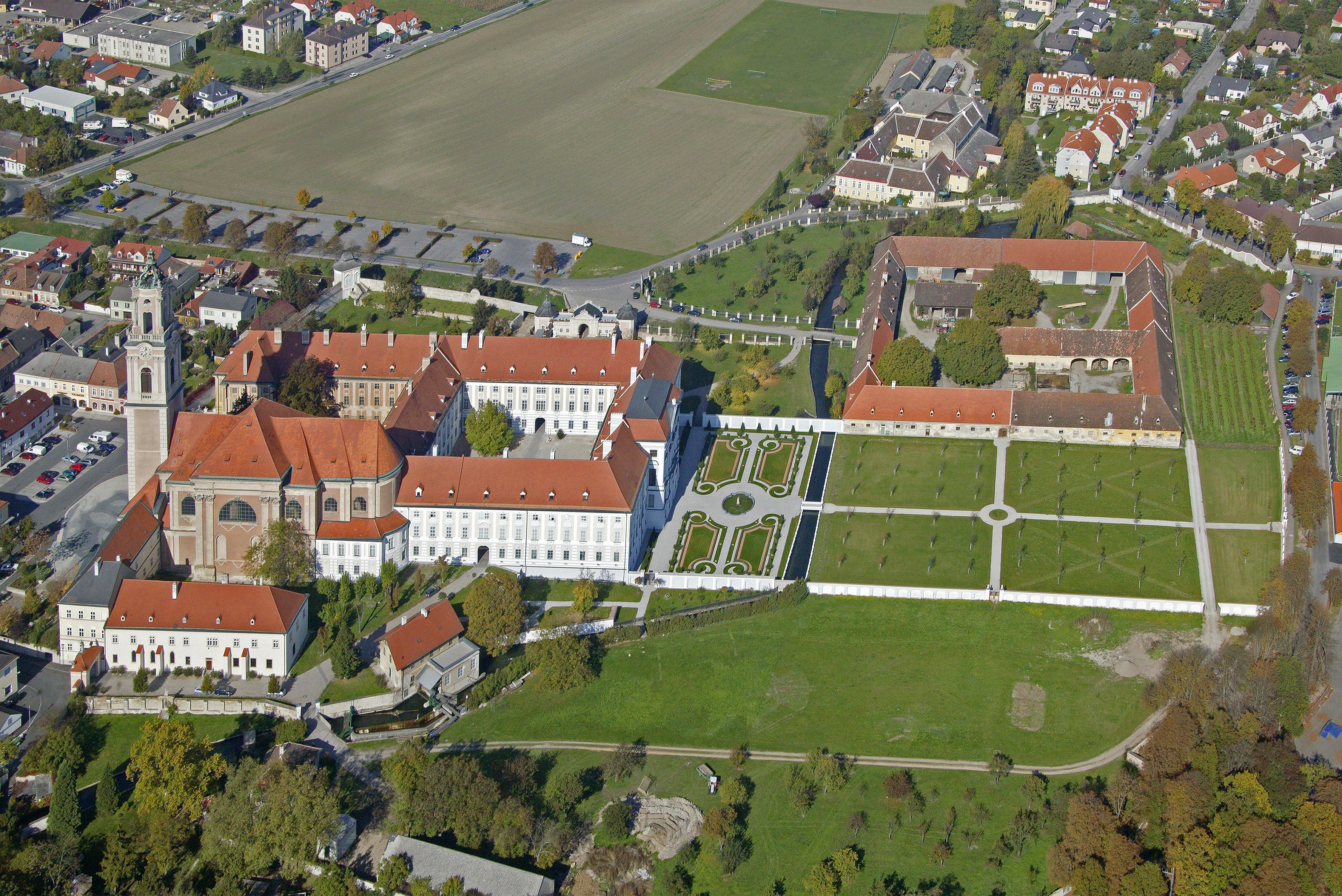 Aerial view of a large building complex with red roofs and gardens.